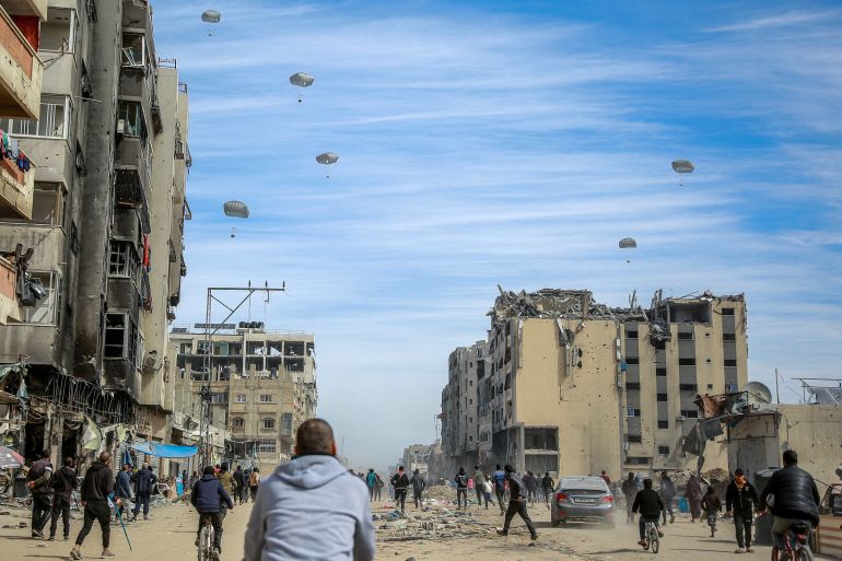 Palestinians run along a street as humanitarian aid is airdropped in Gaza City on March 1