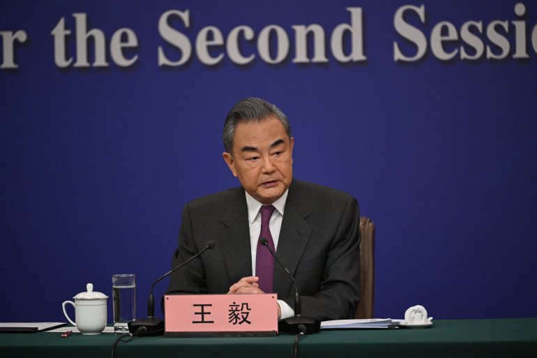 Wang Yi em conferência de imprensa em Pequim.  Ele está sentado em uma mesa.