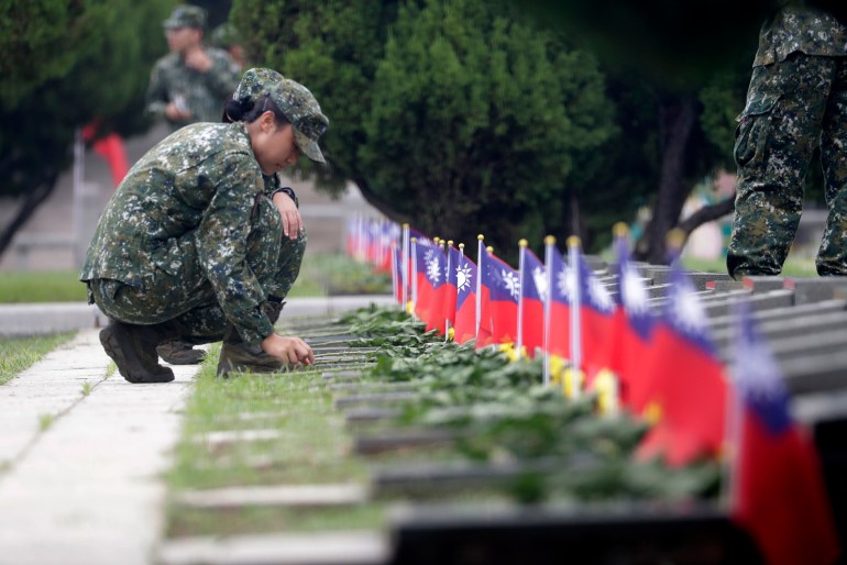 A Taiwan soidier kneeling by the graves of those who died defending Kinmen against China. The grtaves have small Taiwan flags