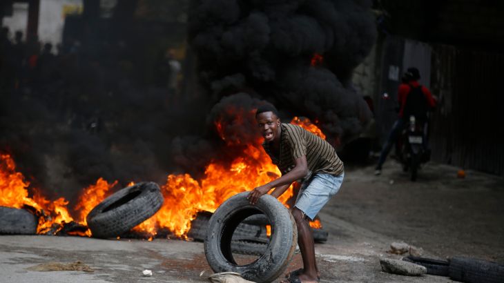 A protester adds tires to a burning barricade during a demonstration demanding the resignation of Prime Minister Ariel Henry