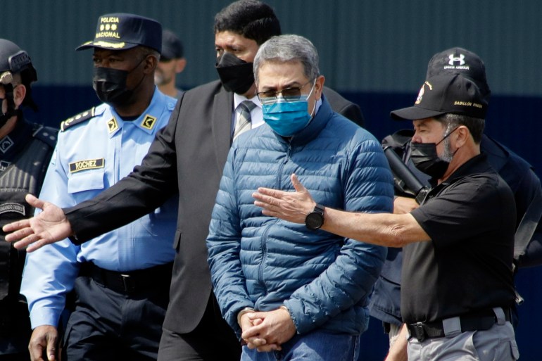 Juan Orlando Hernandez, mit Gesichtsmaske und blauer Daunenjacke, wird von Polizeibeamten eskortiert.