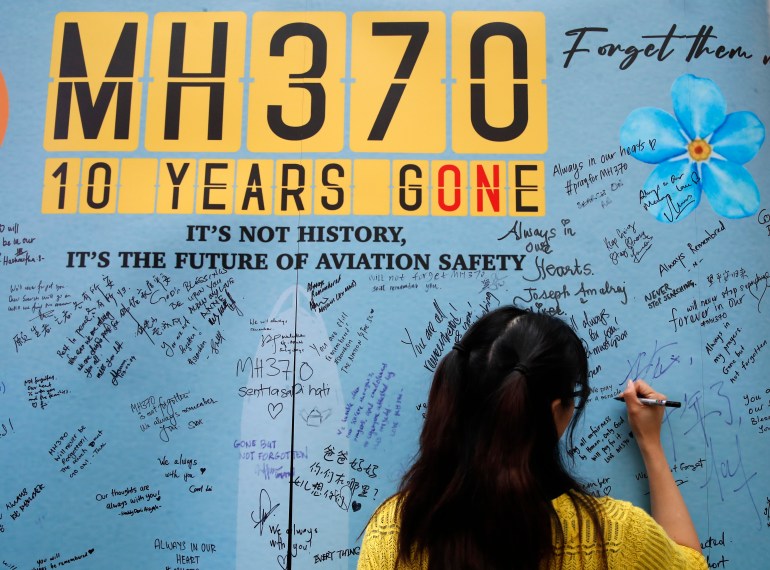 A woman writes a message on a board dedicated to MH370. It has the plane's number and the words '10 years gone'