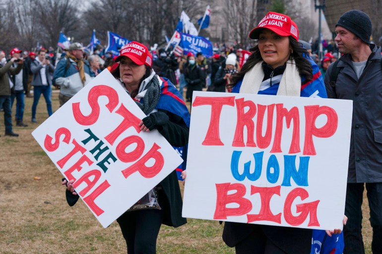 Apoiadores de Trump em 6 de janeiro seguram cartazes que dizem 