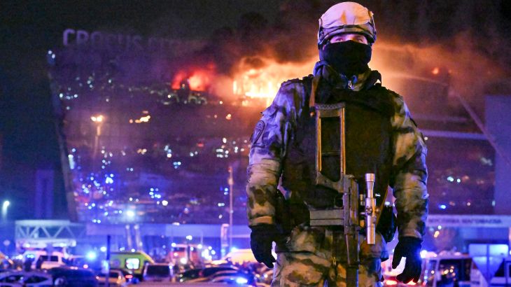 A member of Russia's national guard at the Crocus Concert Hall. The building is behind him in flames.