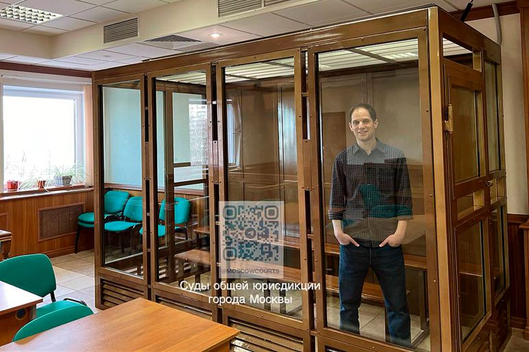 Reporter Evan Gershkovich stands in a glass cage in a courtroom