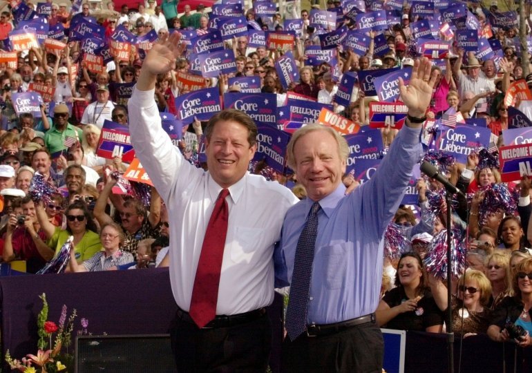 Standing in front⁣ of‍ a crowd of⁣ supporters, Al Gore⁤ and Joe Lieberman wave.