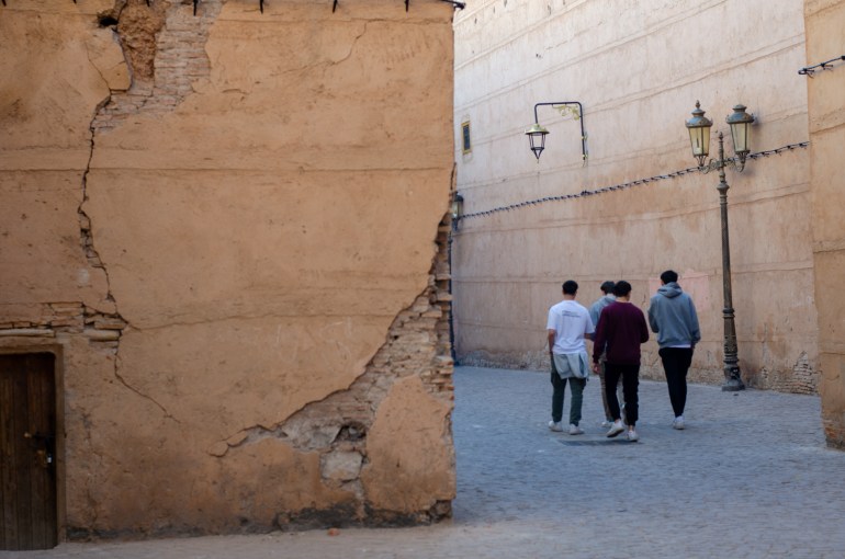 People walk down an alley past damaged wall