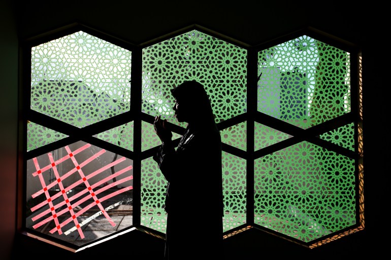 a woman prays in front of green stain glassed windows with one of the windows broken and covered in red tape