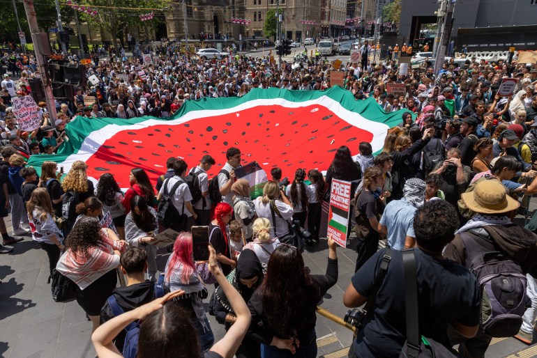people at a protest gather around a large watermelon blanket