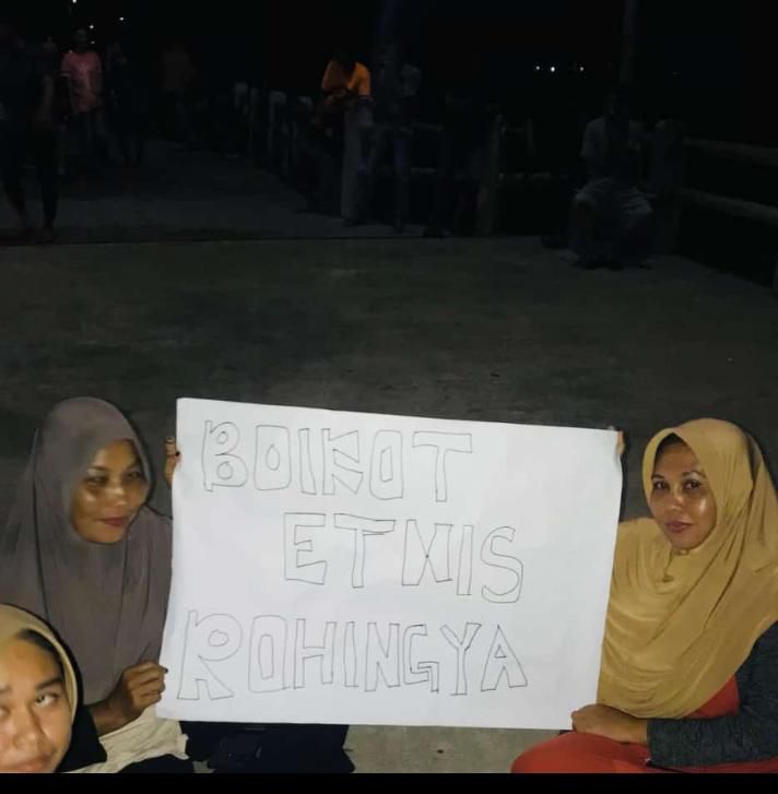 Two women holding a placard reading 'Boycott Rohingya'. The sign is written in Indonesian. 