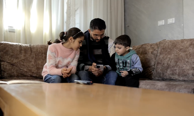 Photo of Jaber with his children Sarah and Omar, looking at photos of Salma on a mobile phone