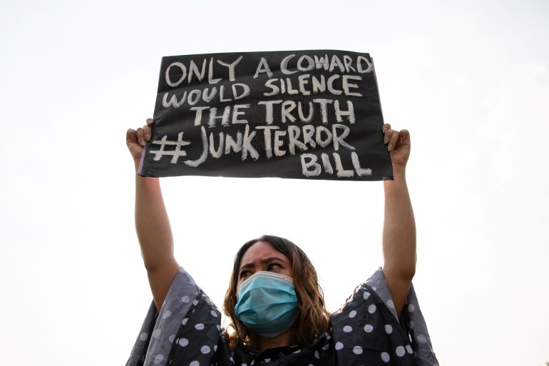 Uma mulher segurando um cartaz durante protestos contra o projeto de lei antiterrorismo.  Sua placa diz 'Só um covarde silenciaria a verdade #junkterrorbill