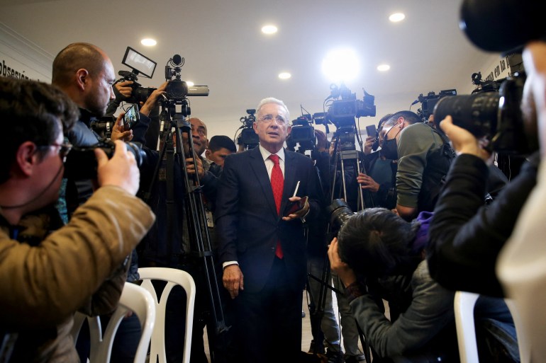 Camera-wielding media members surround and photograph Alvaro Uribe at a news conference.