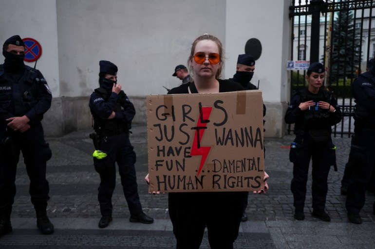 A person stands with a sign next to police officers in front of the Ministry of Health building during a protest, after a pregnant woman died in hospital in an incident campaigners say is the fault of Poland's laws on abortion