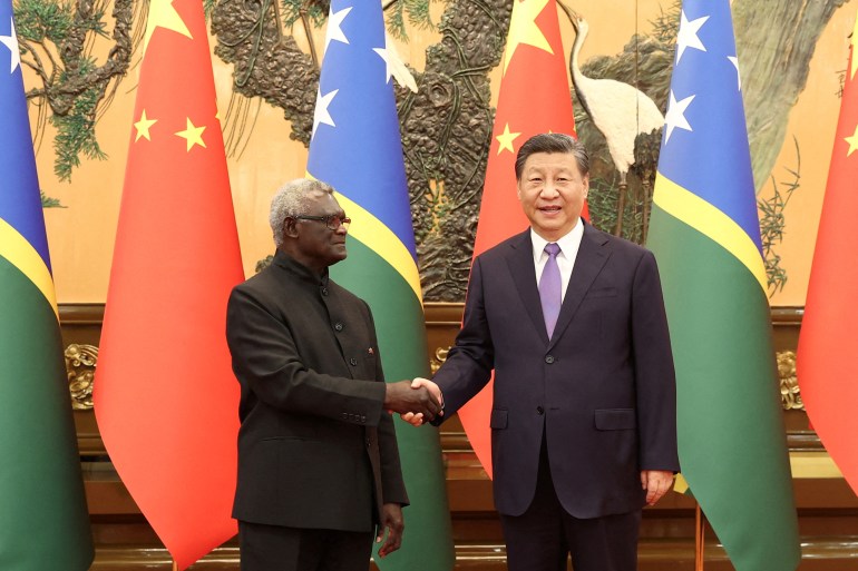 Manasseh Sogavare meeting Xi Jinping in Beijing. They are shaking hands. Xi is smiling. The flags of their two countries are behind them.