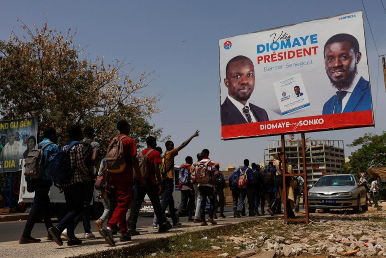 Students walks as they pass an electoral billboard of the Senegalese presidential candidate Bassirou Diomaye Faye, who is backed in the March 24 election by opposition leader Ousmane Sonko, in Dakar, Senegal, March 20, 2024. REUTERS/Luc Gnago