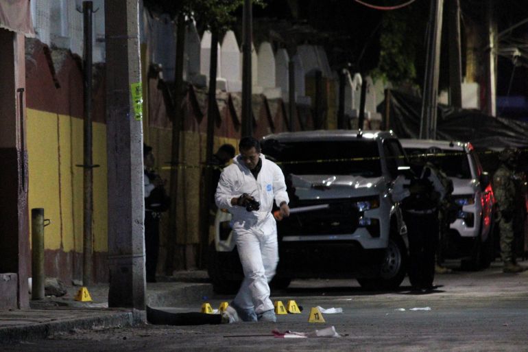 A crime-scene worker, dressed in a white plastic jump suit, walks through evidence markers placed on the street where a shooting occurred.