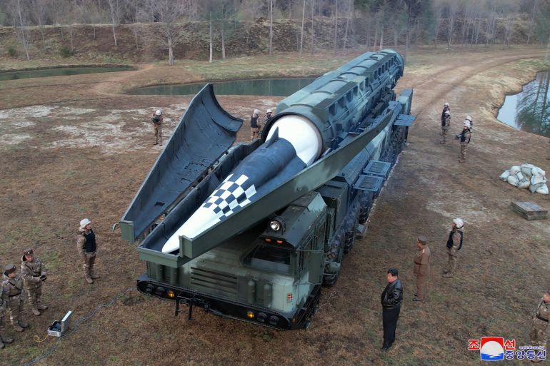 O novo míssil visto de cima.  Ele está em seu transportador antes do lançamento.  Kim Jong Un e alguns oficiais militares estão ao redor.