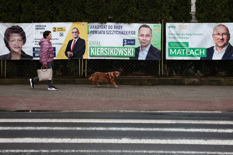 A woman walks with the dog in front of the election posters hanging on the fence, ahead of next weekend Polish local elections, in Szczytno, Poland