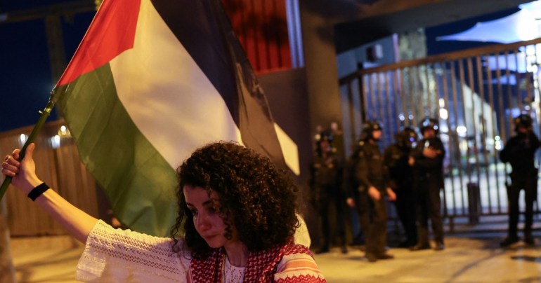 a woman holds a palestinian flag and looks down in sadness