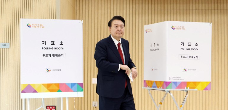 Der südkoreanische Präsident Yoon Suk Yeol geht während der vorgezogenen Abstimmung zwischen zwei Wahlkabinen hindurch.