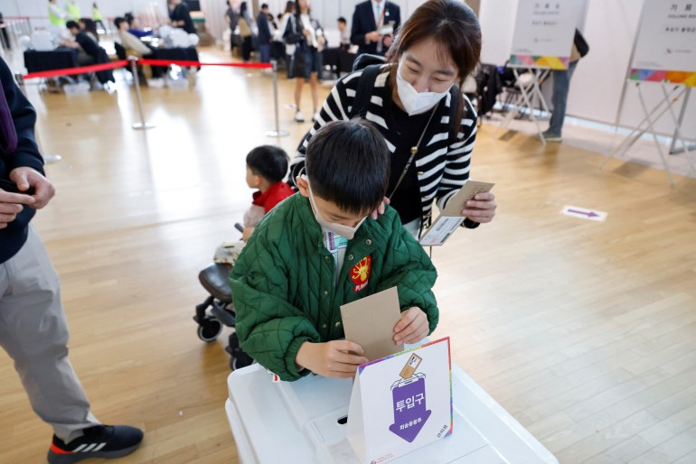 A boy puts his father's ballot paper into the ballot box at an early voting centre in Seoul