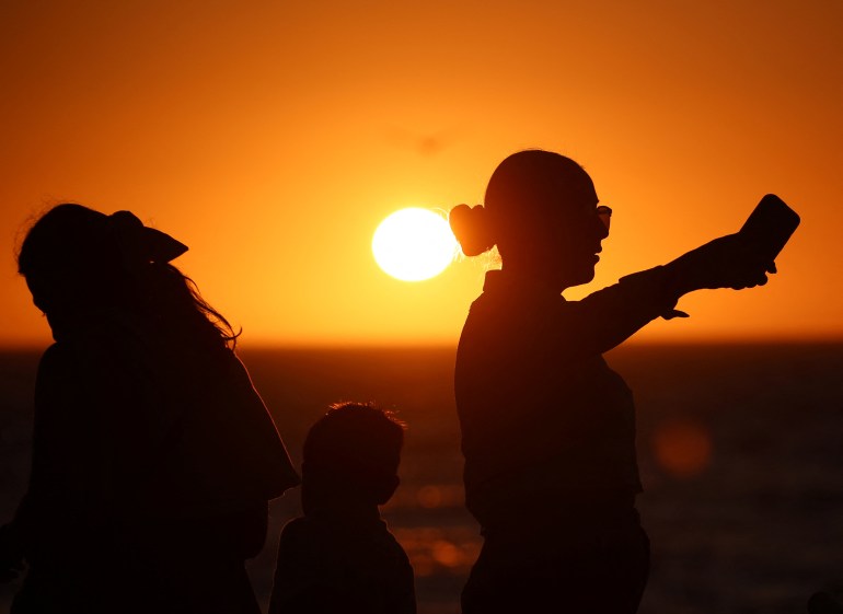 Pessoas aparecem em silhueta ao pôr do sol enquanto visitam o Malecón, um dia antes de um eclipse solar total em Mazatlan, México, 7 de abril de 2024