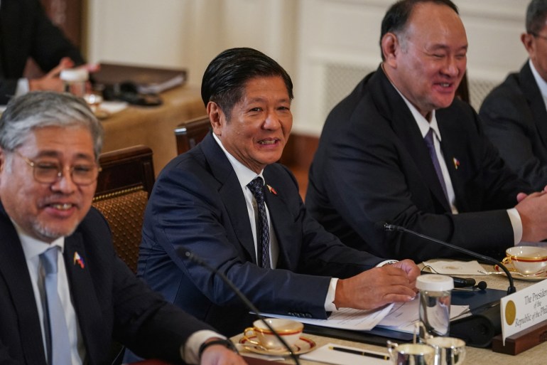 Philippine President Ferdinand Marcos Jr attends a trilateral summit with U.S. President Joe Biden and Japan Prime Minister Fumio Kishida. He is sitting at a table between two of his officials. They are smiling.