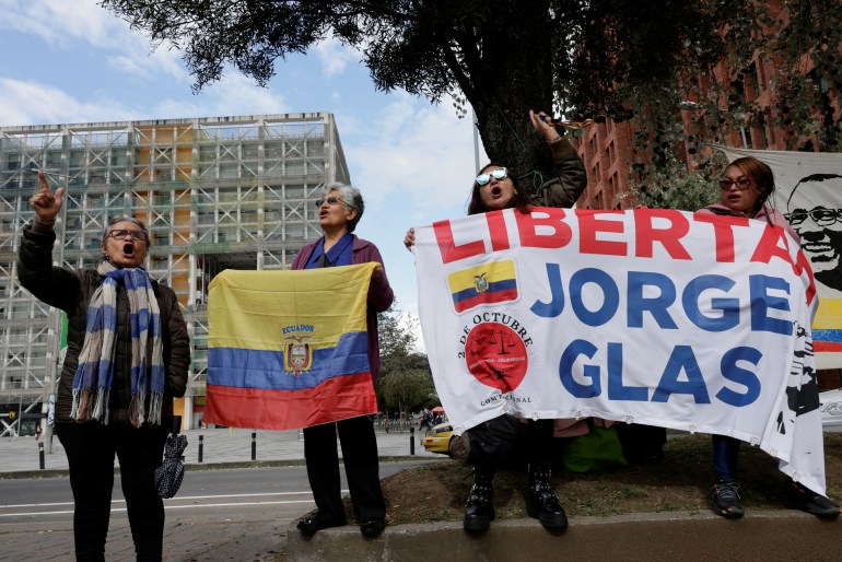 Protesters hold up an Ecuadorian flag and a banner that reads, in Spanish, 
