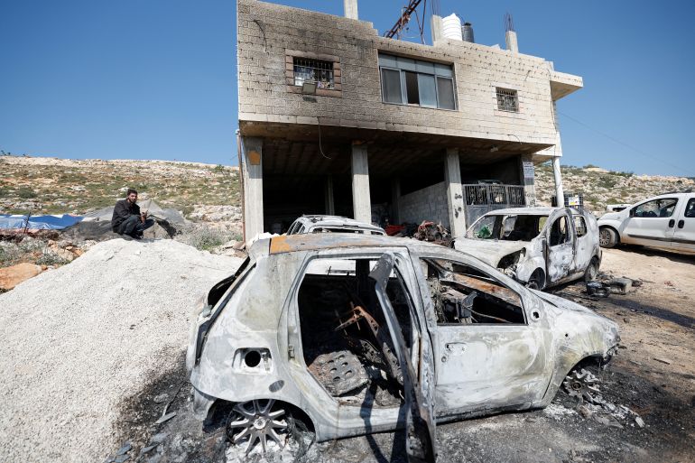 A Palestinian man sits near a damaged house and damaged cars after Israeli settlers attacked the village of al-Mughayyer, in the Israeli-occupied West Bank, April 13, 2024