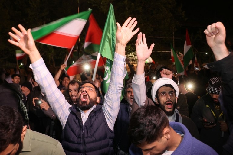 men raise their arms at a protest at night with palestinian flags