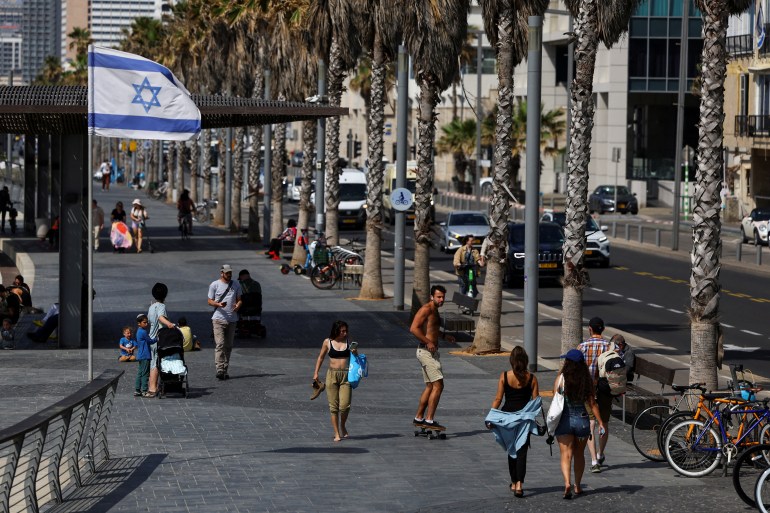 people skateboard on a boulevard next to an Israeli flag