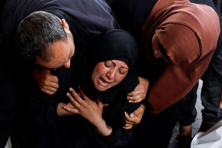 people hold a woman as she mourns