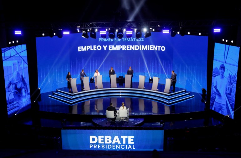 A view of a debate stage in Panama, where eight candidates prepare to discuss policy from behind silver podiums.