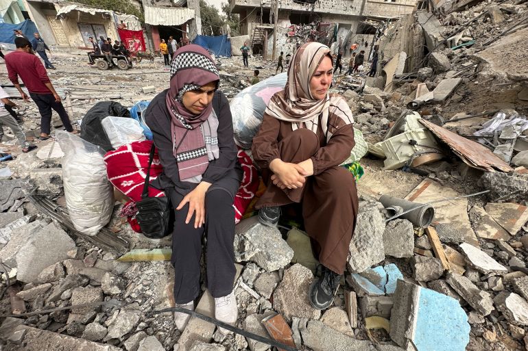 Palestinian women react as they sit on the rubble of a residential building housing their apartments, following an Israeli raid, in Nuseirat,
