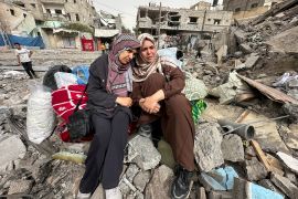 Palestinian women react as they sit on the rubble of a residential building housing their apartments, following an Israeli raid [Doaa Rouqa/Reuters]