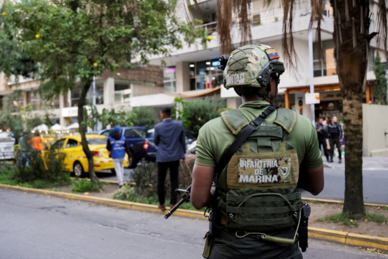 An armed soldier in a helmet stands guard on a Quito city street.