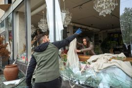 Ukrainians remove shards of glass from the broken windows of a shop damaged by a Russian attack in Kharkiv [Sofiia Gatilova/Reuters]