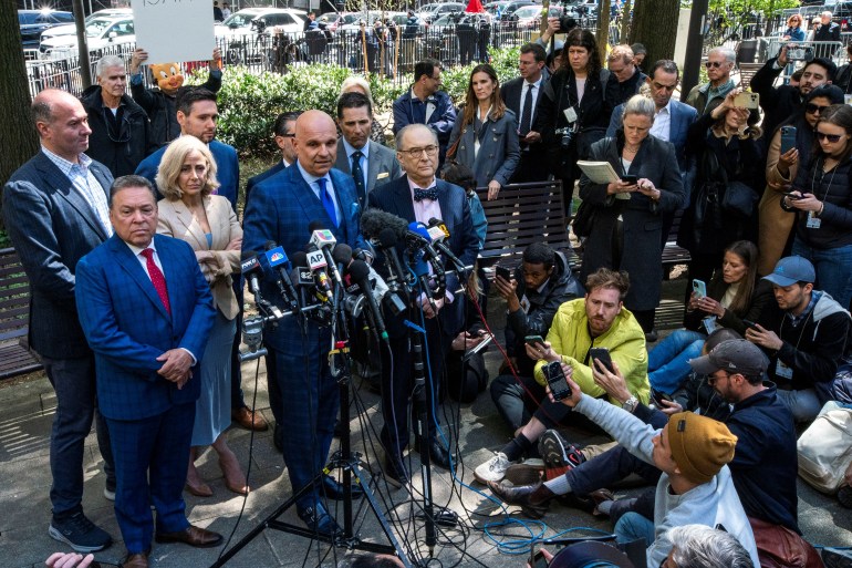 Harvey Weinstein's lawyer Arthur Aidala speaking to the media after the New York court ruling, He is wearing a blue suit and is bald. He is standing in front of a bank of microphones. Others are standing beside him. Some of the journalists are squatting down in front.