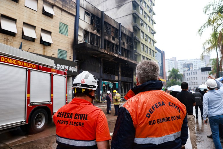 اعضای دفاع مدنی در محل آتش‌سوزی مرگبار در یک مهمانخانه در پورتو آلگره ایستاده‌اند