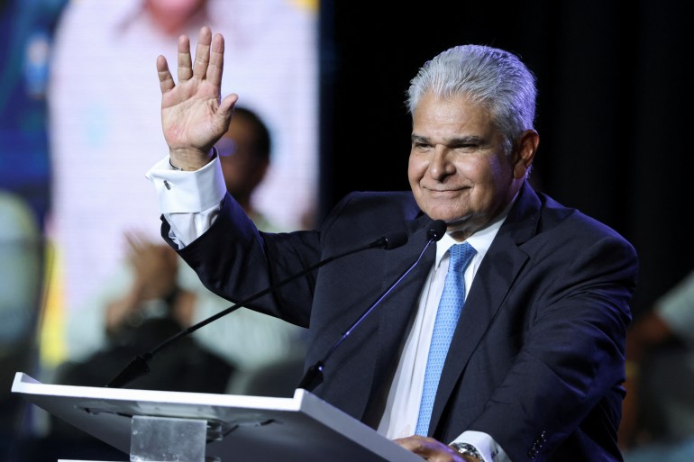 Jose Raul Mulino, dressed in a suit and tie, waves from a podium.