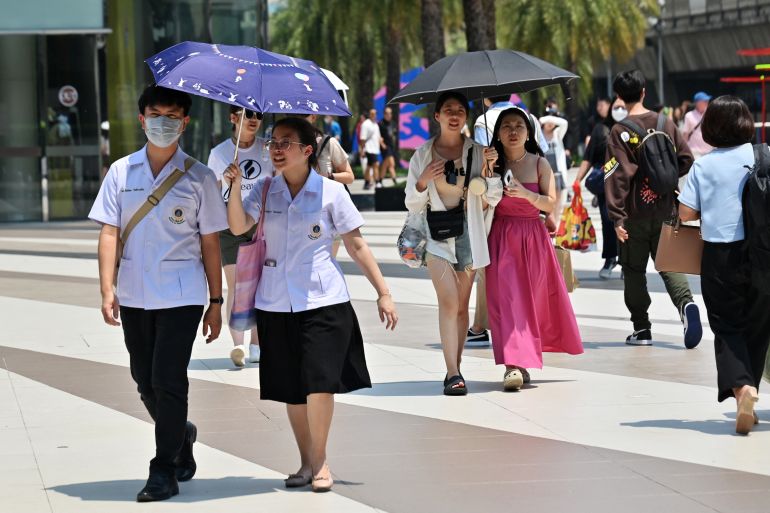 Pedestrians in Bangkok shield themselves from the sun under umbrellas