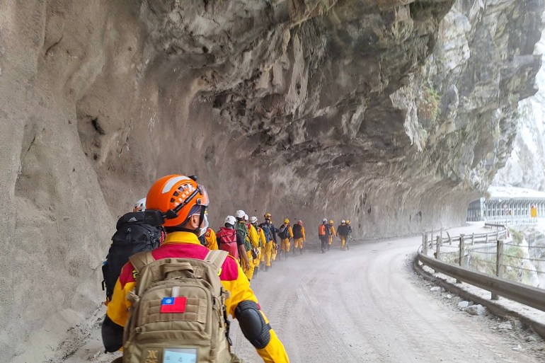 Rescue teams walking beneath a massive rocky outcrop over a road