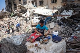 A Palestinian youth prepares a meal while people look for salvageable items amid the rubble of buildings destroyed during Israeli bombardment in Khan Yunis [AFP]