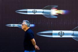 A man walks past a banner depicting missiles along a street in Tehran [AFP]