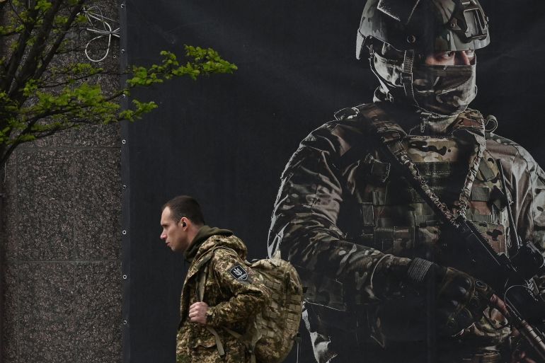 A Ukrainian solider walking past a recruitment poster in Kyiv