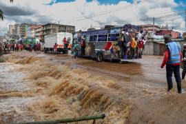 Pedestrians hang off the back of a bus to avoid having to wade across a flooded section of a road in Nairobi. [Tony Karumba/AFP]