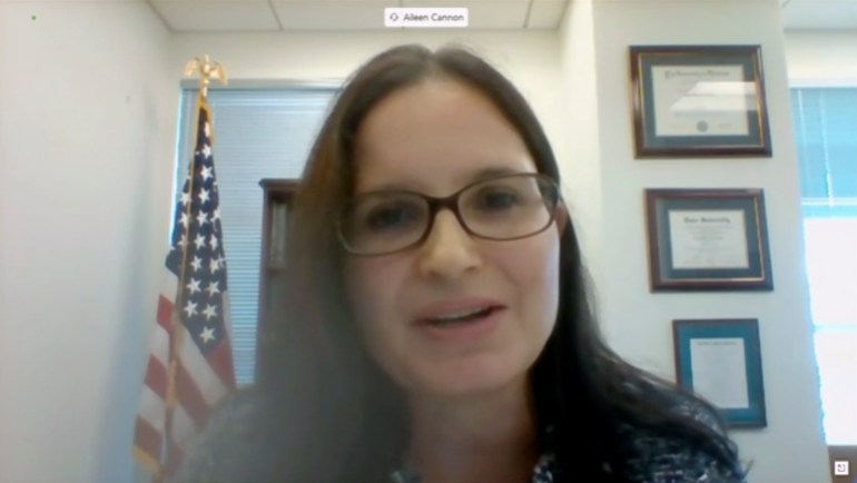 A screenshot of Aileen Cannon in a Zoom meeting. She faces the camera, speaking, a US flag visible in the background.
