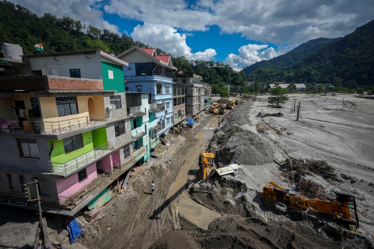 Vehicles that got washed away in floods lie on the sand as machinery is used to clean mud and sand near the buildings along the Teesta river in Rongpo, east Sikkim, India