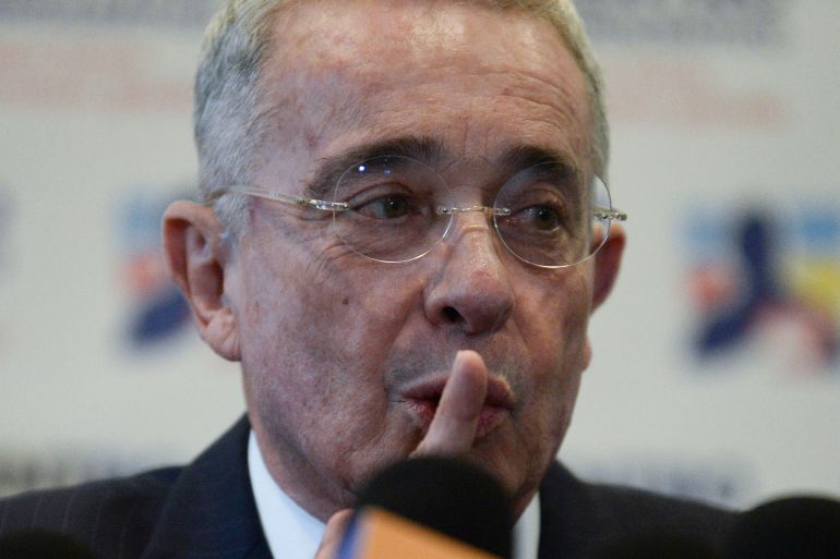 Alvaro Uribe holds a finger up to his mouth